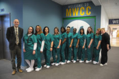 12 people stand in a line. The 10 students in the middle are dressed in nurses outfits.