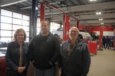 Three people stand in a row in an automotive repair area.